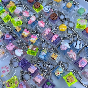 Puede incluir: Una colección de llaveros acrílicos transparentes con varios dijes en miniatura. Los dijes incluyen balones deportivos, postres, animales y otros diseños lindos. Cada llavero tiene un anillo de metal plateado.