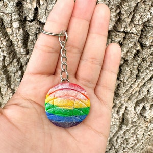 May include: Rainbow-colored volleyball keychain with a silver chain. The keychain is made of polymer clay and has a sparkly finish.