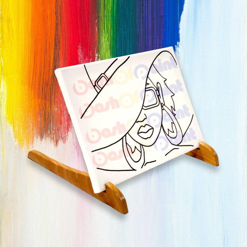May include: A black and white line drawing of a person wearing a large hat and sunglasses. The drawing is on a white canvas and is propped up on a wooden easel.