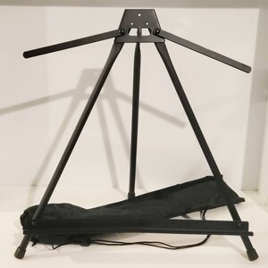 May include: A black metal easel with a carrying case. The easel is adjustable and folds down for easy storage.