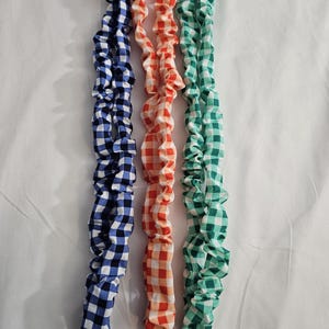 May include: Three fabric lanyards in blue and white, orange and white, and green and white gingham patterns. Each lanyard has a metal ring and a black fabric loop at the bottom. The lanyards are arranged vertically against a white background.