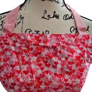 May include: Pink and red heart patterned apron with pink straps.