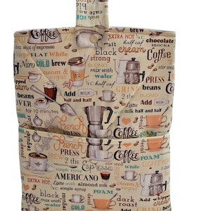 Puede incluir: Un bolso tote beige con temática de café con varios textos e ilustraciones relacionados con el café. La bolsa tiene un bolsillo y un asa, con palabras como "espresso", "latte" y "crema" impresas en ella. El diseño incluye tazas de café y equipos de elaboración.