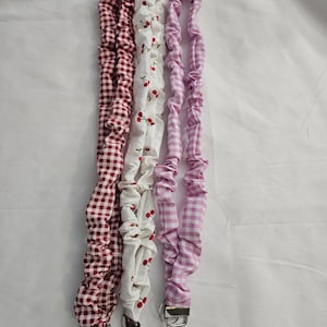 May include: Three fabric lanyards with metal key rings. One is red and white gingham, one is white with red cherries, and the third is pink and white gingham. The lanyards are made of gathered fabric.