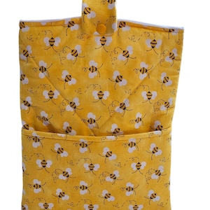 May include: Yellow fabric organizer with a bee pattern. The organizer has a pocket and a flap that fastens with a yellow button. The bee pattern features black and white bees with dotted flight paths on a yellow background.