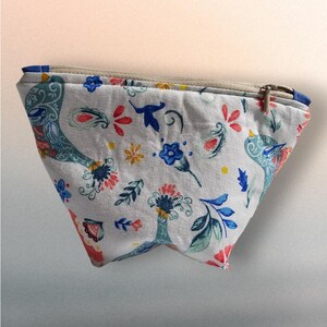 May include: A white fabric pouch with a zipper closure. The pouch is decorated with a colorful floral and bird pattern. The pattern includes blue, green, red, yellow, and white colors.