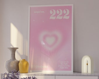May include: Aesthetic interior scene featuring a white cabinet with gold hardware, a pink coffee table, and a pink chair. A framed poster with the number 222 and a heart design hangs above the cabinet. A vase of purple flowers and a decorative lamp are also visible.