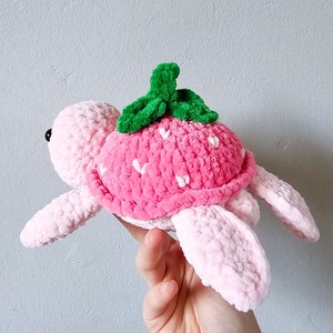 May include: A pink crocheted turtle with a strawberry-shaped shell and green leaves on top.