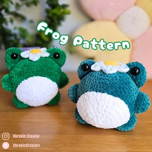 May include: Two plush frog toys, one green and one teal, with white bellies and daisy crowns. The text "Frog Pattern" is written in green. The frogs have large black eyes. The toys are handmade.