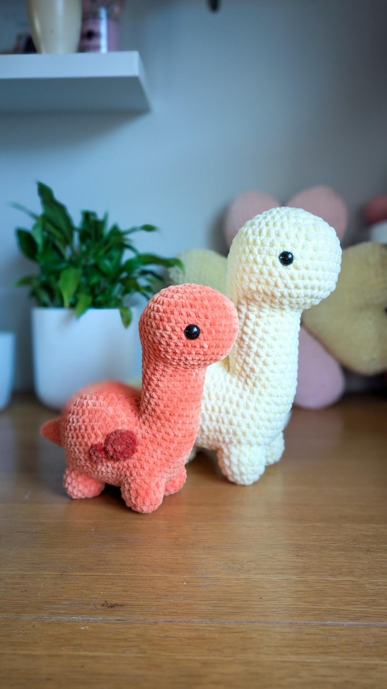 Pu&ograve; includere: Due giocattoli di dinosauro all'uncinetto, uno &egrave; di colore arancio chiaro e l'altro &egrave; di colore crema. Entrambi i dinosauri hanno gli occhi neri.