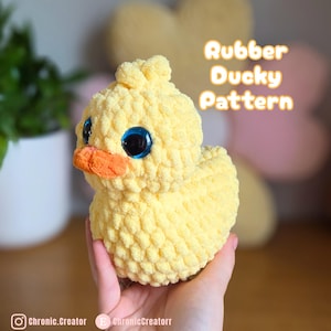 Puede incluir: Un pato de ganchillo amarillo hecho a mano con grandes ojos azules y un pico naranja. El texto "Rubber Ducky Pattern" se muestra en naranja. El pato es un juguete de peluche suave.