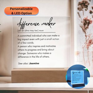 May include: A white acrylic sign with the word "difference maker" defined as "a committed individual who can make a big impact even with just a small action of a few words." The sign is on a wooden base and has a small LED light.