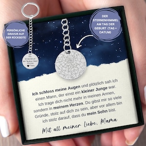 May include: A silver necklace with a round pendant featuring a star map. The pendant is in a black box with a white background and text that reads "DER STERNENHIMMEL AM TAG DER GEBURT (TAG + DATUM)" and "Ich schloss meine Augen und plötzlich sah ich einen Mann, der einst ein kleiner Junge war. Ich trage dich nicht mehr in meinen Armen, sondern in meinem Herzen. Du gibst mir so viele Gründe, stolz auf dich zu sein, aber vor allem bin ich stolz darauf, dass du mein Sohn bist. Mit all meiner Liebe, Mama".