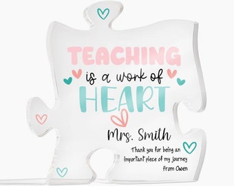 May include: A white acrylic puzzle piece with the text "TEACHING is a work of HEART" in pink and blue lettering. The text "Mrs. Smith" is written below the heart with the message "Thank you for being an important piece of my journey From Owen" in smaller text.