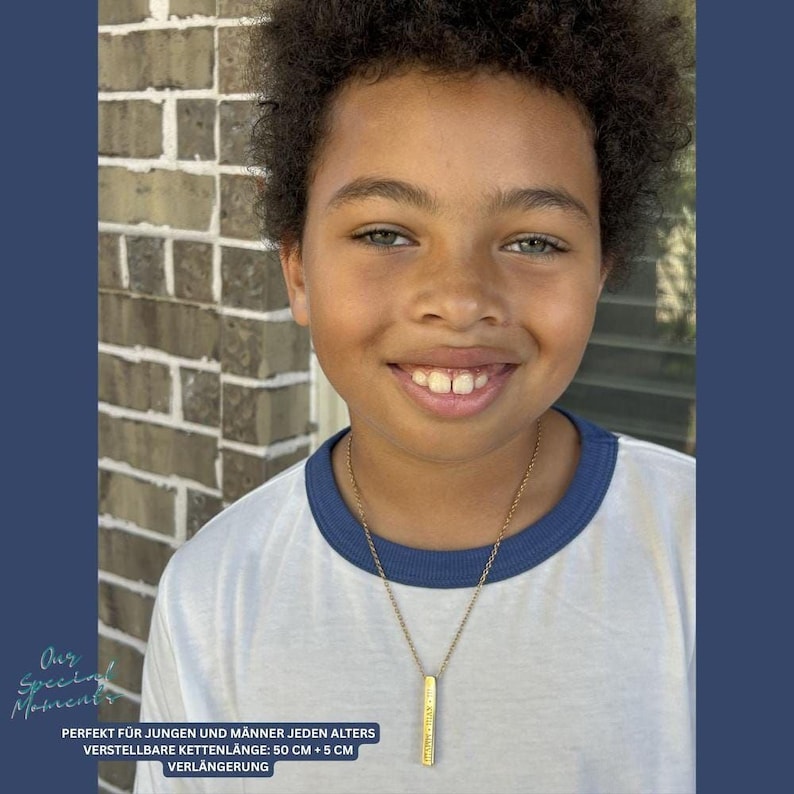 A young boy with curly hair is smiling at the camera, wearing a white shirt and a necklace.