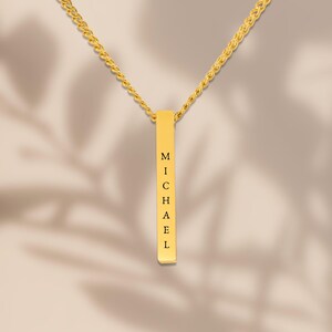 A gold necklace with a rectangular pendant that has the name "Michael" engraved on it.