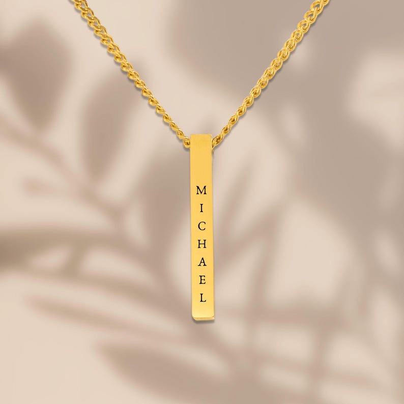 A gold necklace with a rectangular pendant that has the name "Michael" engraved on it.