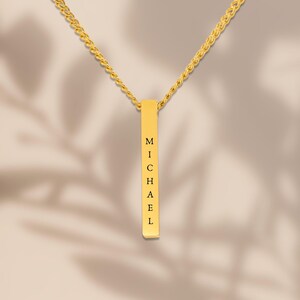 A gold necklace with a rectangular pendant that has the name "Michael" engraved on it.