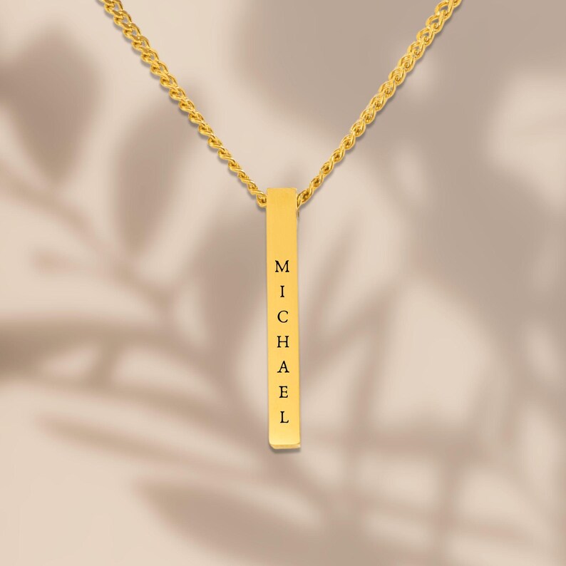 A gold necklace with a rectangular pendant that has the name "Michael" engraved on it.