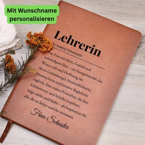 May include: A brown leather-bound notebook with the German word "Lehrerin" (teacher) printed on the cover. The notebook has text in German and the name "Frau Schuster" at the bottom. A sprig of orange flowers rests on the notebook.