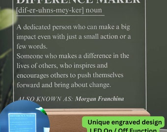 Op de afbeelding: Een witte acrylplaat met een zwarte inscriptie die "Difference Maker" luidt, met een definitie en de woorden "Also Known As: Morgan Franchina". De plaat wordt verlicht met groene LED-verlichting en staat op een houten voet. De plaat heeft een uniek gegraveerd ontwerp en een LED aan/uit-functie.