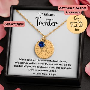 Op de afbeelding: Gouden ketting met een ronde hanger met een blauwe edelsteen en een gegraveerd zonneradiatie-ontwerp. De ketting wordt gepresenteerd in een zwarte doos met Duitse tekst, waaronder "Für unsere Tochter" en "Geburtsstein".