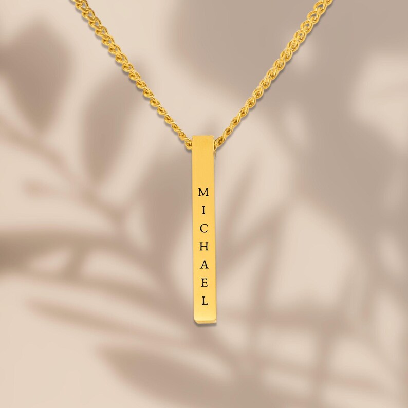A gold necklace with a rectangular pendant that has the name "Michael" engraved on it.
