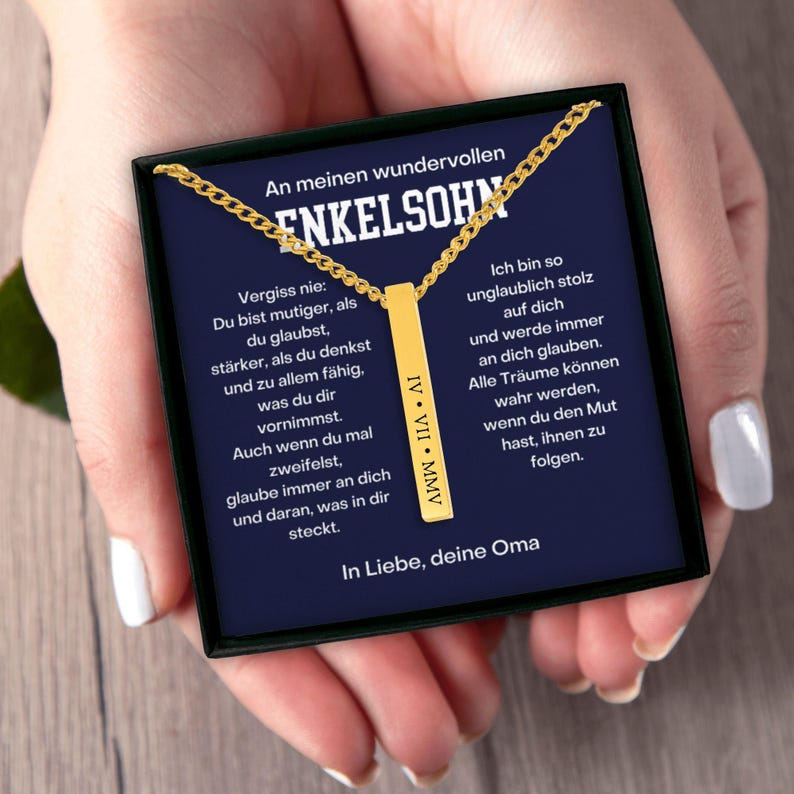 a person's hand holding a black box with a gold chain necklace. The box contains a message in German, which appears to be a personal message or a gift.