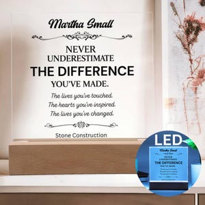May include: A clear acrylic plaque with black text reading Martha Small, NEVER UNDERESTIMATE THE DIFFERENCE YOU'VE MADE. The lives you've touched. The hearts you've inspired. The lives you've changed. Stone Construction, set on a wooden base.