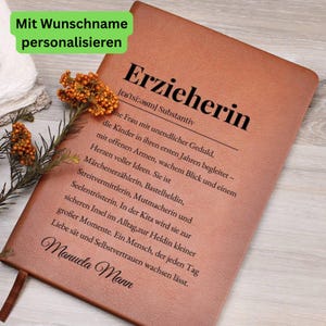 May include: A brown leather-bound journal with the German word "Erzieherin" embossed on the cover. The journal features a definition and a personalized name. A sprig of orange flowers rests on the side.