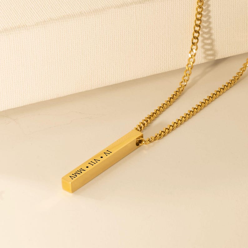 A gold-colored necklace with a rectangular pendant that has the text "AVWV" engraved on it.