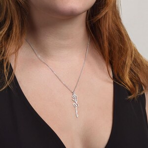A close-up of a woman wearing a silver necklace with a pendant that says "Came".