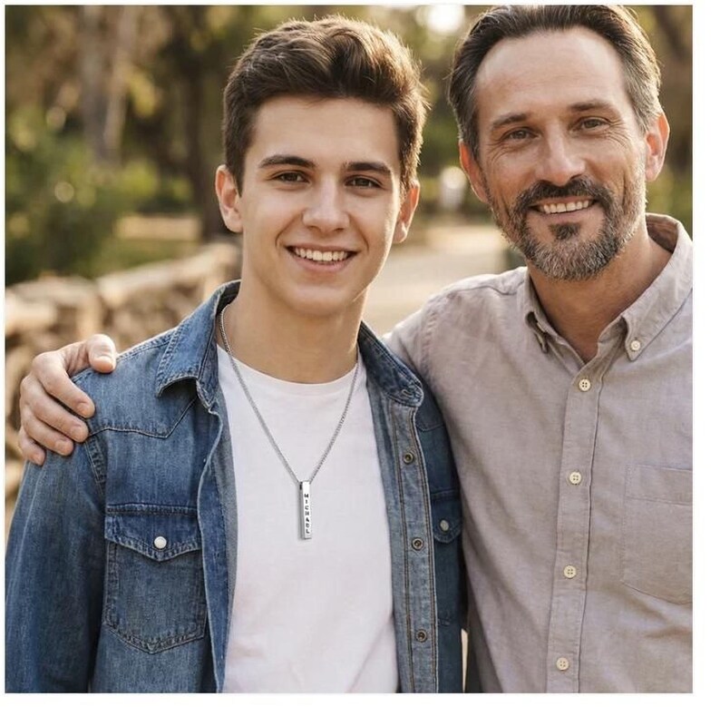 A young man and an older man stand together, smiling and embracing each other.
