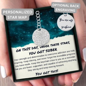 May include: A silver keychain with a star map charm and a black box with the text "On this day, under these stars, you got sober". The box also includes the text "Your strength and determination to overcome addiction are truly inspiring. Keep shining, and never forget the incredible progress you have made. Keep this keychain close to you as a reminder that you are loved, supported, and capable of achieving anything. Stay strong and keep moving forward. You got this!"