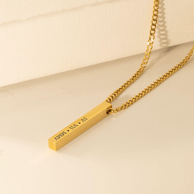 A gold-colored necklace with a rectangular pendant that has the text "AVWV" engraved on it.