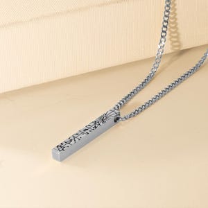 A silver necklace with a rectangular pendant featuring a design or text.