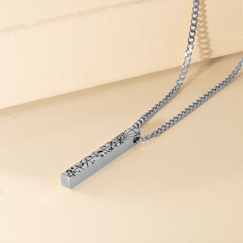 A silver necklace with a rectangular pendant featuring a design or text.