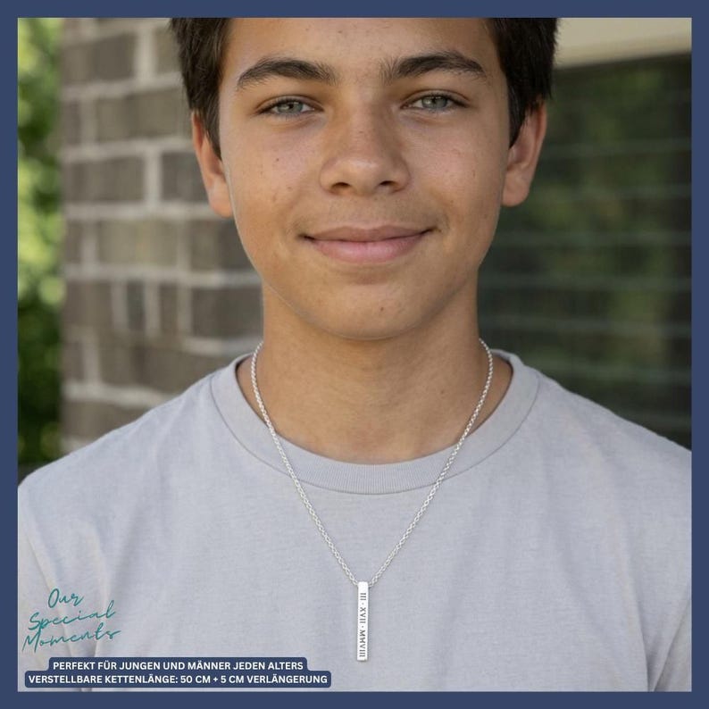A young man wearing a gray t-shirt and smiling at the camera, with a silver necklace around his neck.