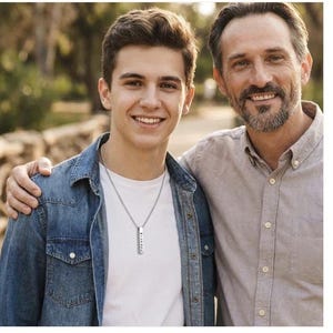 A young man and an older man stand together, smiling and embracing each other.