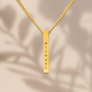 A gold necklace with a rectangular pendant that has the name "Michael" engraved on it.