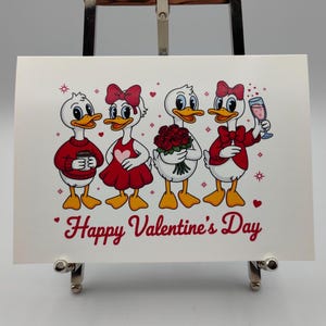 May include: A Valentine's Day card featuring four cartoon ducks. The ducks are dressed in red and white outfits, holding a coffee cup, flowers, and a glass of wine. The words "Happy Valentine's Day" are written in red script.