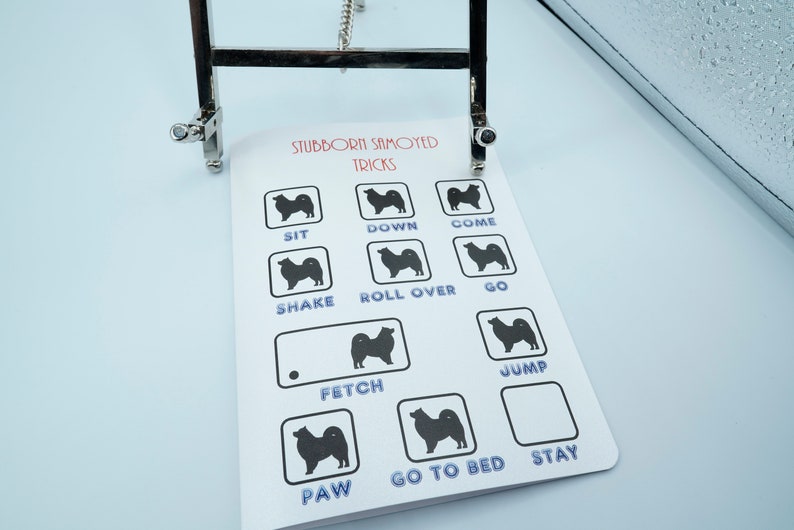 May include: A white card with black silhouettes of Samoyed dogs and the text "Stubborn Samoyed Tricks" at the top. The card lists various dog tricks such as "Sit", "Down", "Come", "Shake", "Roll Over", "Go", "Fetch", "Jump", "Paw", "Go to Bed", and "Stay".