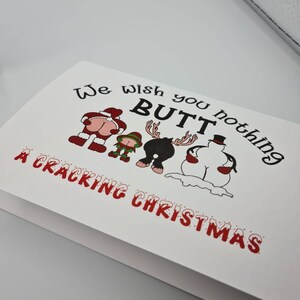 Peut inclure: Carte de No&euml;l blanche avec le texte &laquo;&nbsp;We wish you nothing BUTT a Cracking Christmas&nbsp;&raquo;. La carte pr&eacute;sente des illustrations de dessins anim&eacute;s du P&egrave;re No&euml;l, d'un elfe, d'un renne et d'un bonhomme de neige, chacun avec son post&eacute;rieur expos&eacute;.