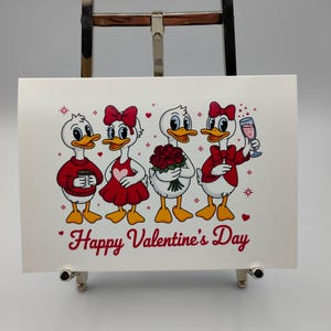 May include: A white Valentine's Day card featuring four cartoon ducks. Each duck is dressed in red and white, holding a coffee cup, a heart-shaped dress, a bouquet of roses, and a glass of pink champagne. The words "Happy Valentine's Day" are written in red.