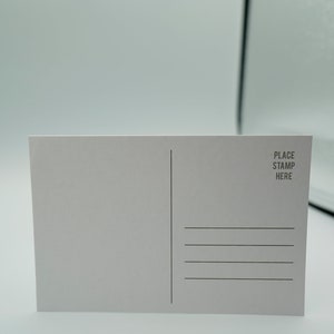 May include: A blank white postcard with a line down the middle and four lines for writing on the right side. The text "PLACE STAMP HERE" is printed in the top right corner.
