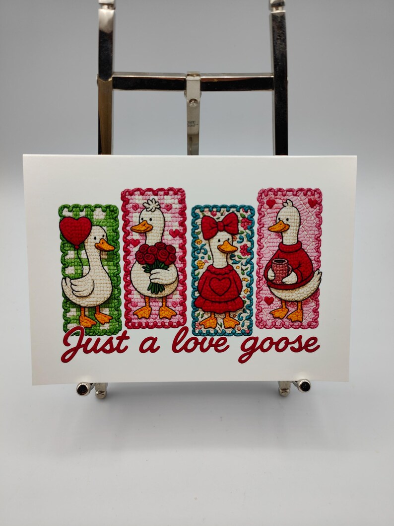 May include: A white card featuring four embroidered geese in rectangular frames. Each goose has a different accessory: a heart, flowers, a bow, and a mug. The text "Just a love goose" is written in red script below the geese.
