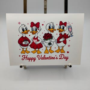 May include: A Valentine's Day card featuring four cartoon ducks. The ducks are dressed in red and white outfits, holding a bouquet of roses and a glass of wine. The words "Happy Valentine's Day" are written in red.