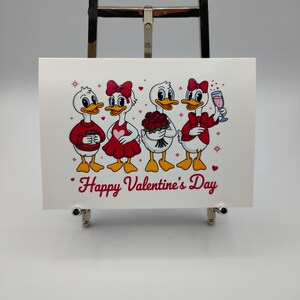 May include: A Valentine's Day greeting card featuring four cartoon ducks. Each duck is dressed in red and white attire, holding a coffee cup, wearing a heart-shaped dress, holding roses, and holding a glass of wine. The words "Happy Valentine's Day" are written in red.
