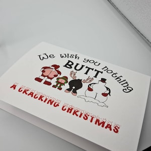 Peut inclure: Carte de No&euml;l blanche avec le texte "We wish you nothing BUTT a Cracking Christmas." La carte pr&eacute;sente des images de dessins anim&eacute;s du P&egrave;re No&euml;l, d'un elfe, d'un renne et d'un bonhomme de neige, chacun avec son post&eacute;rieur expos&eacute;.