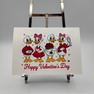 May include: A Valentine's Day greeting card featuring four cartoon ducks. The ducks are dressed in red and white outfits, holding a coffee cup, flowers, and a glass of champagne. The words "Happy Valentine's Day" are written in red script.